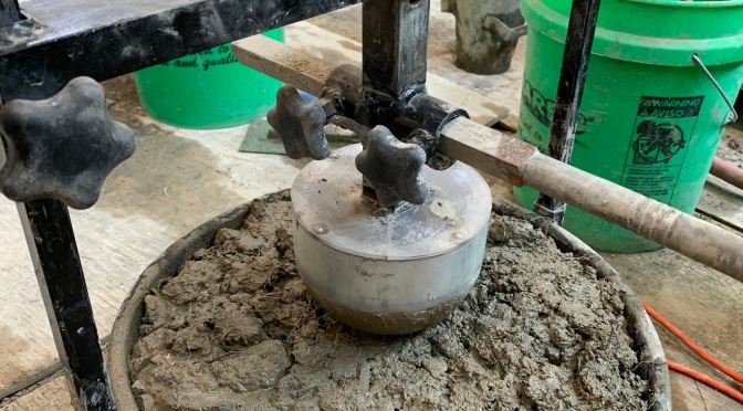 V-Kelly test apparatus: wet concrete in a large, round container with a mixing arm that has a large hardened concrete ball on the end.