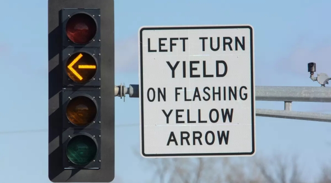 Traffic signal with four heads vertically aligned. The second head is lit as a yellow arrow. A sign to the right of the signal reads “Left Turn Yield on Flashing Yellow Arrow.”