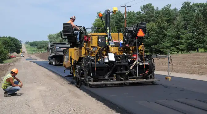 Road crew lays pavement on rural road.